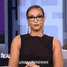 A Woman Wearing Glasses And A Black Tank Top Is Sitting On A Couch And Smiling . GIF