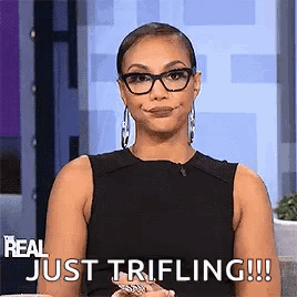 A Woman Wearing Glasses And A Black Tank Top Is Sitting On A Couch And Smiling . GIF
