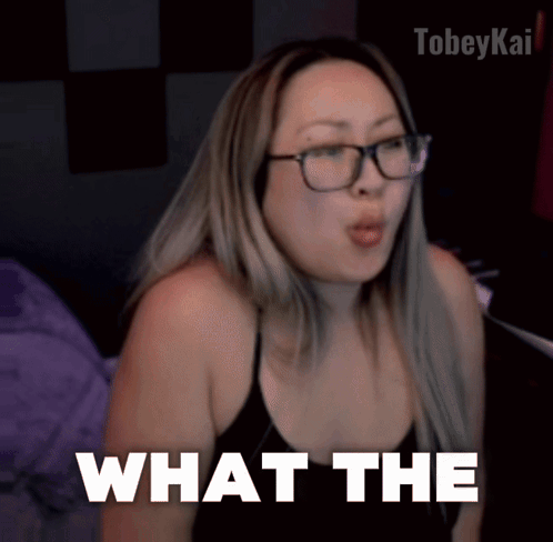 A Woman Wearing Glasses And A Black Top Says What The GIF