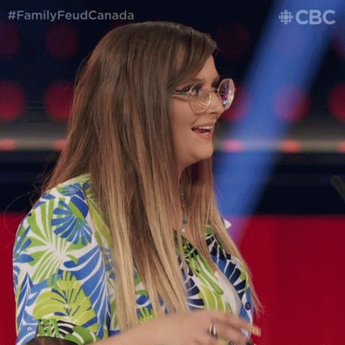 A Woman Wearing Glasses And A Blue And Green Shirt With The Words Family Feud Canada Behind Her GIF