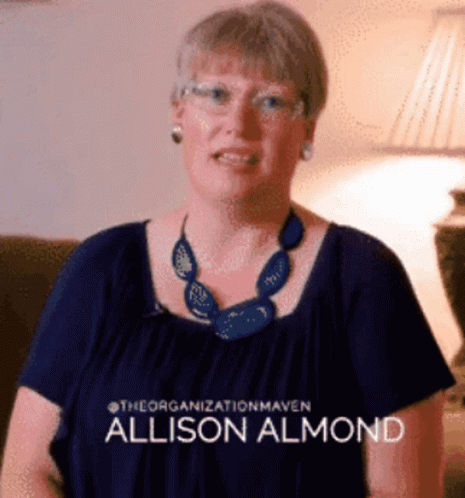 a woman wearing glasses and a blue necklace has the name allison almond on her shirt