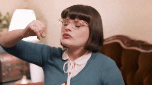 A Woman Wearing Glasses And A Blue Sweater Is Pointing GIF