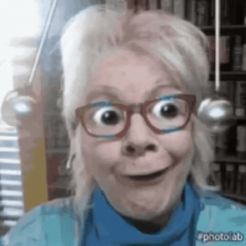 A Woman Wearing Glasses And A Blue Sweater Is Smiling For The Camera GIF
