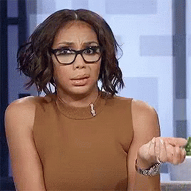 A Woman Wearing Glasses And A Brown Tank Top Is Making A Face . GIF