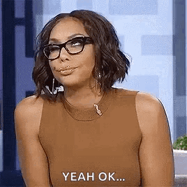 A Woman Wearing Glasses And A Brown Tank Top Is Sitting In Front Of A Camera And Saying Yeah Ok . GIF