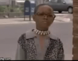A Woman Wearing Glasses And A Choker Is Standing In Front Of A Brick Building . GIF