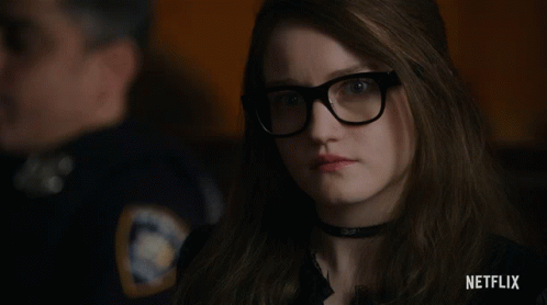 A Woman Wearing Glasses And A Choker With A Netflix Logo Behind Her GIF