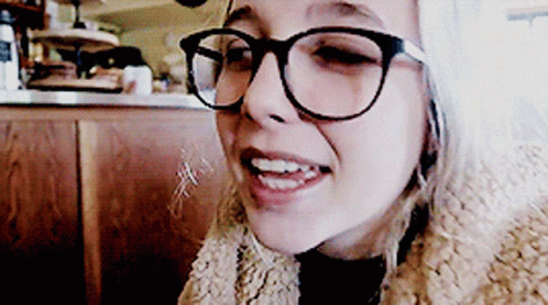 A Woman Wearing Glasses And A Fur Coat Smiles At The Camera GIF