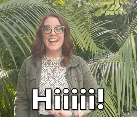 A Woman Wearing Glasses And A Green Jacket Is Standing In Front Of A Palm Tree And Smiling . GIF