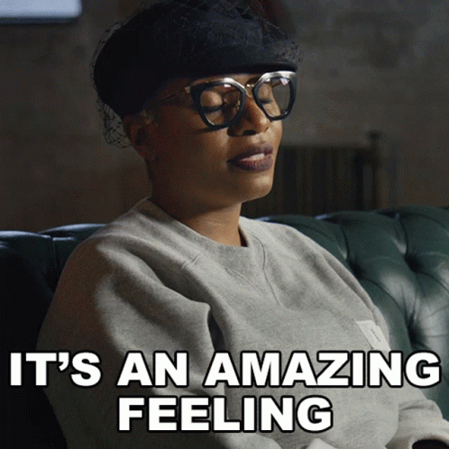 A Woman Wearing Glasses And A Hat Is Sitting On A Couch With The Words It 'S An Amazing Feeling Above Her GIF
