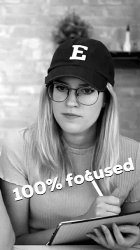 A Woman Wearing Glasses And A Hat With The Letter E On It Is 100 % Focused GIF