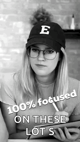 A Woman Wearing Glasses And A Hat With The Letter E On It Says 100 % Focused On These Lots GIF