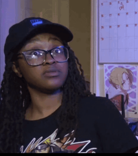 A Woman Wearing Glasses And A Hat With The Letter T On It Is Standing In Front Of A Calendar GIF
