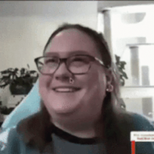 A Woman Wearing Glasses And A Nose Ring Is Smiling . GIF