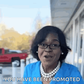 A Woman Wearing Glasses And A Pearl Necklace Is Talking To Someone . GIF