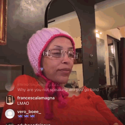 A Woman Wearing Glasses And A Pink Hat Is Sitting In Front Of A Mirror GIF