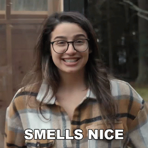 A Woman Wearing Glasses And A Plaid Shirt Smiles And Says " Smells Nice " GIF