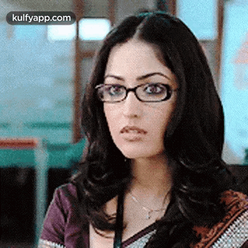 A Woman Wearing Glasses And A Purple Shirt Is Looking At The Camera . GIF