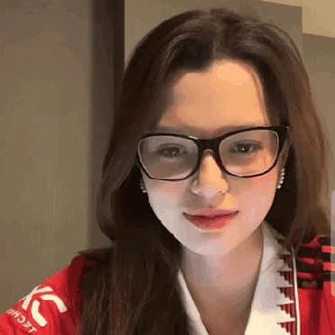 A Woman Wearing Glasses And A Red Jacket Is Looking At The Camera . GIF