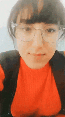 A Woman Wearing Glasses And A Red Sweater Looks At The Camera GIF