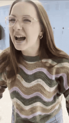 A Woman Wearing Glasses And A Striped Sweater Is Laughing With Her Mouth Open GIF