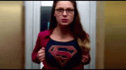A Woman Wearing Glasses And A Superman Cape Is Standing In An Elevator . GIF