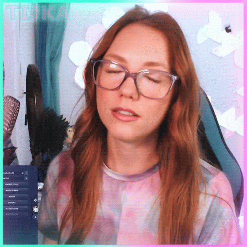 A Woman Wearing Glasses And A Tie Dye Shirt Is Sitting In Front Of A Computer Screen With The Word Tika Written On It GIF