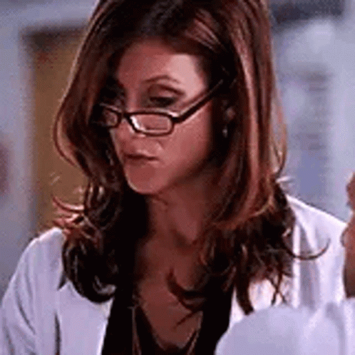 A Woman Wearing Glasses And A White Lab Coat Is Looking Down . GIF