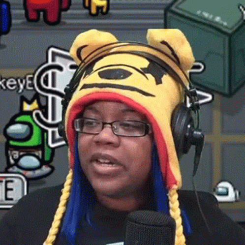 A Woman Wearing Glasses And A Winnie The Pooh Hat Is Talking Into A Microphone . GIF