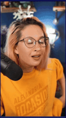A Woman Wearing Glasses And A Yellow Shirt That Says Alexandria Tucasio GIF