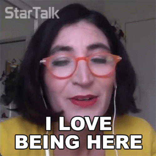 A Woman Wearing Glasses And Ear Buds Says I Love Being Here GIF