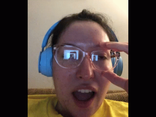 A Woman Wearing Glasses And Headphones Holds Her Hand To Her Face GIF