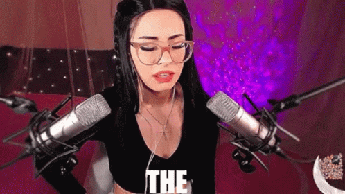 A Woman Wearing Glasses And Headphones Is Standing In Front Of A Microphone And Says The . GIF