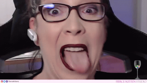 A Woman Wearing Glasses And Red Lipstick Is Sticking Her Tongue Out . GIF