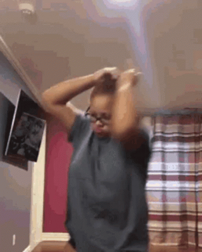 A Woman Wearing Glasses Is Dancing In A Room With Her Hands In Her Hair . GIF