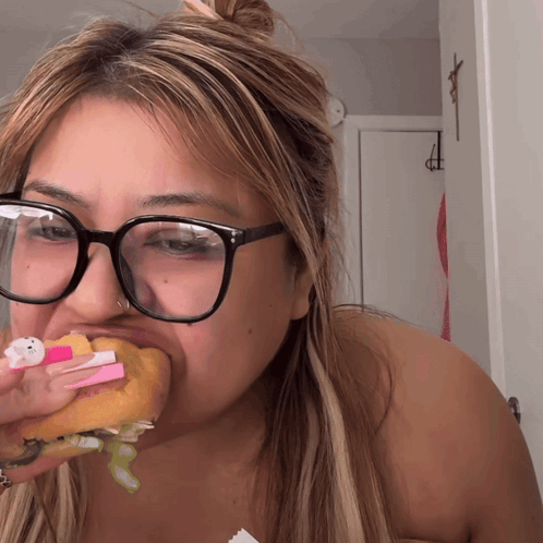 a woman wearing glasses is eating a donut