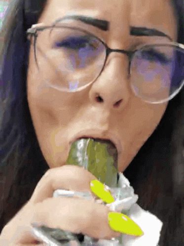 A Woman Wearing Glasses Is Eating A Pickle With Her Tongue GIF