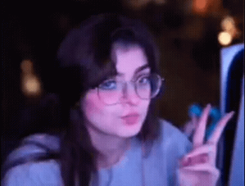 a woman wearing glasses is giving a peace sign while looking at a computer screen .