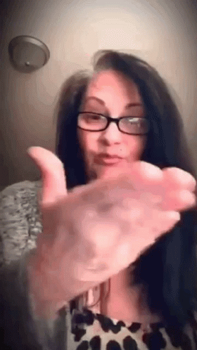 A Woman Wearing Glasses Is Giving A Thumbs Up With Her Hand . GIF