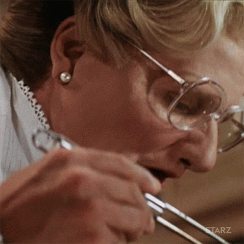 A Woman Wearing Glasses Is Holding A Pair Of Scissors In Her Mouth GIF