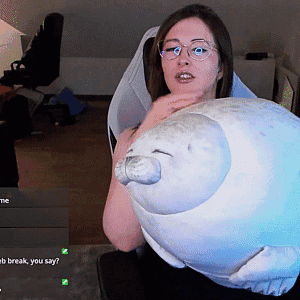 A Woman Wearing Glasses Is Holding A Stuffed Seal In Her Hands GIF