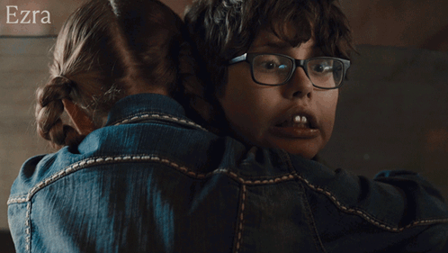 a woman wearing glasses is hugging another woman wearing a blue shirt with the name ezra on the bottom