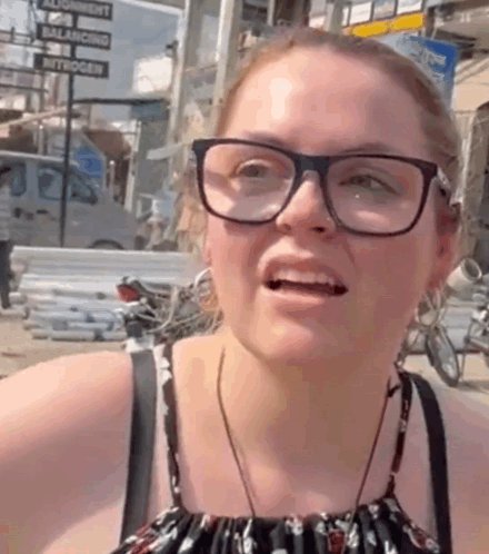 A Woman Wearing Glasses Is Making A Funny Face In Front Of A Sign That Says Balance GIF