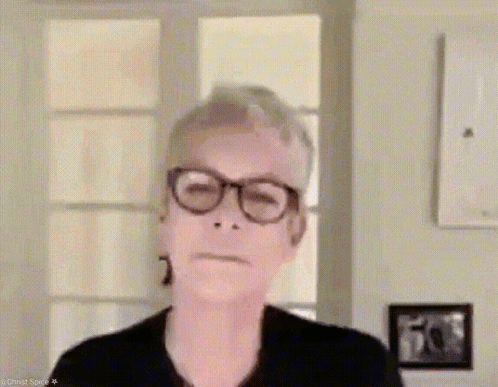 A Woman Wearing Glasses Is Making A Funny Face While Standing In Front Of A Window . GIF