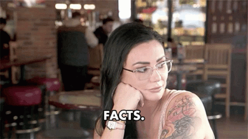 A Woman Wearing Glasses Is Sitting At A Table With Her Hand On Her Chin And Says Facts . GIF
