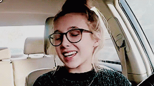 A Woman Wearing Glasses Is Sitting In A Car And Smiling GIF