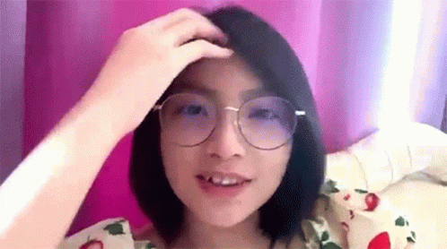 A Woman Wearing Glasses Is Sitting On A Bed . GIF