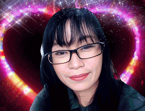 A Woman Wearing Glasses Is Smiling In Front Of A Heart GIF