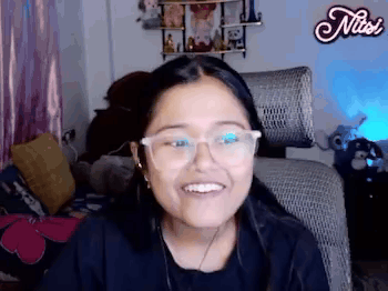 A Woman Wearing Glasses Is Smiling While Sitting In A Chair In A Room . GIF