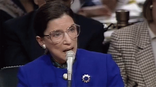 A Woman Wearing Glasses Is Speaking Into A Microphone GIF
